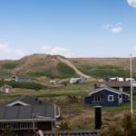 Dorf mit Häusern und Wohnwagen vor Dünen unter blauem Himmel.