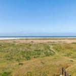 Weitläufiger Blick auf Strand und Meer mit grasbewachsenen Dünen im Vordergrund.