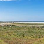 Weitläufiger Strand mit Dünen und klarem Himmel. Menschen genießen die Landschaft.