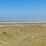 Weitläufige Dünenlandschaft mit Blick auf das Meer unter blauem Himmel.