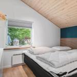 Schlafzimmer mit Bett, Fenster und Holzdecke. An der Wand hängt ein Kleiderhaken.