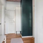 Flur mit Holzboden, weißer Tür und grüner Wand. Kleiner Teppich und Schrank sichtbar.