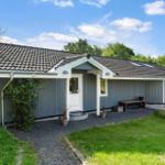 Ein Haus mit grauer Fassade, weißer Tür und Dach mit Schiebedachfenstern. Umgeben von Gras und Bäumen.