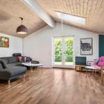 Wohnzimmer mit Holzdecke, Sofa, Sessel und Fenster zur Grünfläche.