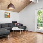 Wohnzimmer mit grauem Sofa, Holzboden und Fenster zur Außenterrasse.