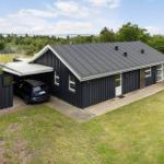 Black house with garage, terrace, and view of forest and water.