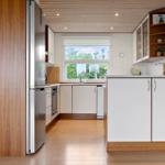 Modern kitchen with wooden floor, white cabinets, and stainless steel refrigerator.