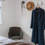A bed, chair, and robe hang on a wall with hooks and a window.