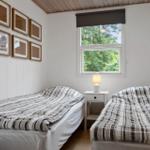 Two beds with striped bedding, a nightstand with lamp, and a window with a view of trees.