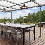 Deck with large table, chairs, and heaters under canopy. Background: forest and hot tub.