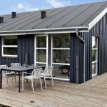 Modern wooden cabin with terrace and seating area. Large windows and roof vents.