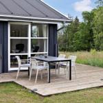 Deck with table and chairs in front of a house with dark wood and glass windows.