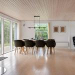 Dining area with wooden floor, large windows, and dining table with chairs. Fireplace in foreground.