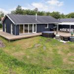 Modern wooden cabin with terrace, hot tub, and grill area in green surroundings.