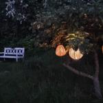 Eine weiße Bank steht im Garten unter Bäumen mit hängenden Lampen.