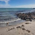 Strand mit Steinen und Sand, Meer und Himmel im Hintergrund.