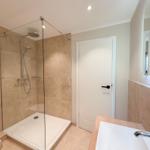 Badezimmer mit Dusche, Waschbecken und Toilette. Wandfliesen und Spiegel.