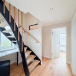 Treppe mit Holzgeländer und Sitzbank neben Fenster. Holzboden und helle Wände.