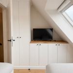 Schlafzimmer mit Dachschrägen, TV und Fenster. Weiße Schränke und Holzboden.