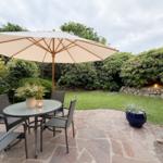 Garten mit Tisch, Stühlen und Sonnenschirm auf Steinplatten.