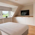 Schlafzimmer mit Dachschrägen, TV, Schrank und Fenster mit Blick auf Grün.