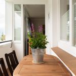 Terrasse mit Holztisch, Stühlen und Pflanze in Metalltopf. Blick auf Außenbereich.