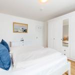Schlafzimmer mit weißem Bett, blauen Kissen und weißen Schränken. Wandbild und Holzboden.
