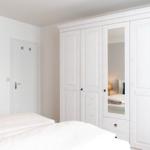 Schlafzimmer mit weißem Schrank und Bett. An der Wand hängt ein Bild.