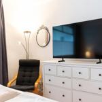 Schlafzimmer mit TV, Schrank und Sessel. Fenster mit Vorhängen.