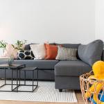 Ein grauer Sofa mit Kissen, zwei Tische und ein Korb mit Spielzeug.