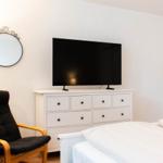 Schlafzimmer mit Bett, TV auf Schrank und schwarzer Sessel.