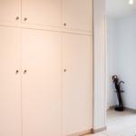 Großer Kleiderschrank mit drei Türen und zwei oberen Schubladen. Blick in einen Flur mit Regenschirmständer.