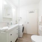 Badezimmer mit Waschmaschine, Spiegelschrank und Heizkörper mit Handtüchern.