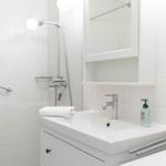 Badezimmer mit Dusche, Waschbecken und Spiegelschrank. Weiße Fliesen und moderne Armaturen.