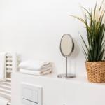 Badezimmer mit Handtuchhalter, gefaltetem Handtuch, Spiegel und Pflanze in Korb.