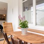 Terrasse mit Holztisch, Stühlen und Blumenkübel. Blick in das Esszimmer.