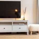 Flachbildfernseher auf weißen Schrank mit Schubladen und Stuhl daneben.
