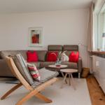 Ein Wohnzimmer mit braunem Sofa, roten Kissen und einem Holzstuhl.
