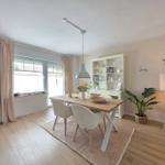 Esszimmer mit Holztisch, Stühlen und Bücherregal an der Wand.