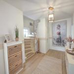 Hausflur mit Holztreppe, Wandbild Leuchtturm und dekorativen Gegenständen auf Möbeln.
