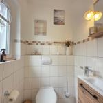 Badezimmer mit Toilette, Waschbecken und Fenster. Wandbilder und Holzregal.