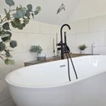 Freistehende Badewanne mit schwarzer Armatur und Pflanzen im Badezimmer.