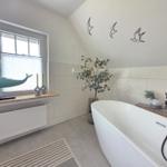 Bad mit freistehender Badewanne, Fenster, Wanddekoration und Pflanzen.