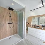 Dusche mit Glaswand und Holzwand, Waschtisch mit Spiegel und Holzplatte