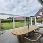 Terrasse mit Holztisch, Stühlen und Sofa. Hintergrund: Grasfläche und Nachbarhäuser.