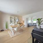 Essbereich mit Tisch, Stühlen und Bücherregal. Wohnzimmer mit Sofa und Kamin im Hintergrund.