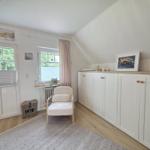Ein Raum mit weißem Schrank, Sessel und Fenstern mit Blick auf Bäume.