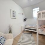 Schlafzimmer mit Doppelstockbett, Sessel und Wandbild. Holzdielenboden und Fenster.
