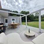 Terrasse mit Sitzgruppe, Esstisch und Grill. Hintergrund: Rasen und Bäume.