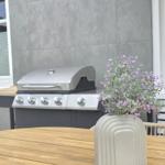 Terrasse mit Grill, Holztisch und Vasenblumen.